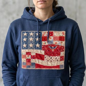 Puede incluir: Sudadera con capucha azul marino con un diseño de bandera americana de patchwork. La bandera incluye estrellas blancas sobre un campo azul y rayas rojas y blancas con estampados florales y paisley. La sudadera tiene una capucha con cordón.