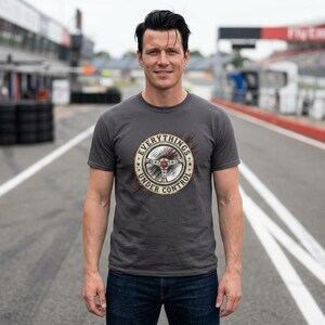 May include: A grey t-shirt with a circular graphic showing a steering wheel and the text "EVERYTHINGS UNDER CONTROL". The person wearing the shirt is standing on a racetrack.