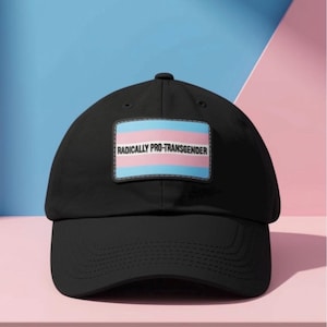 May include: A black baseball cap featuring a rectangular patch on the front. The patch displays the transgender pride flag colours of light blue, pink, and white, with the text RADICALLY PRO-TRANSGENDER printed in black capital letters.