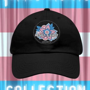 May include: Black baseball cap with a circular patch featuring a floral design in pink and blue, and the words "RESIST & EXIST." The background displays the colors of the transgender pride flag, with the words "TRANS RIGHTS COLLECTION" in neon-style lettering.
