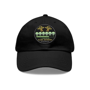 Pode incluir: Boné de beisebol preto com um patch circular com um gráfico verde e amarelo de alienígenas e discos voadores. O texto no patch diz "LOADING... ALIEN INVASION". O boné tem uma aba curva e uma alça ajustável.