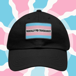 May include: Black baseball cap with a rectangular patch featuring the transgender pride flag colors and the text "RADICALLY PRO-TRANSGENDER". The background has a pattern of light blue and pink shapes.