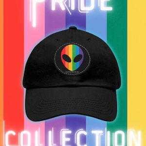 May include: A black baseball cap featuring a circular patch on the front. The patch displays a rainbow-coloured alien head graphic with black eyes and the text CRYPTID REALM INC. The cap is set against a vertical rainbow striped background with neon text.