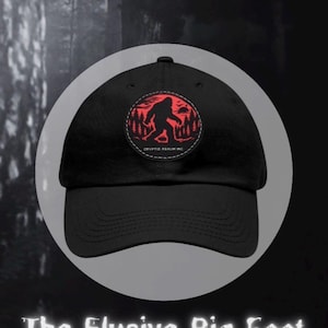 May include: A black baseball cap featuring a circular patch on the front. The patch displays a red silhouette of a creature resembling Bigfoot walking through a forest under a red sun, with the text CRYPTID REALM INC. printed below the figure.