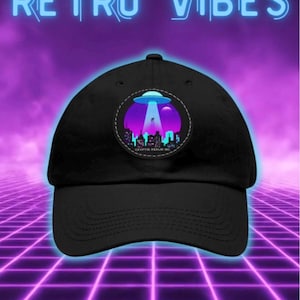 Pode incluir: Um boné de beisebol preto com um emblema circular na frente. O emblema exibe um gráfico de um OVNI pairando sobre o horizonte de uma cidade com um céu em gradiente roxo e azul. O texto RETRO VIBES aparece em azul acima do boné na imagem.