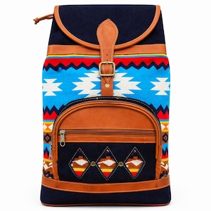 May include: A navy blue backpack with a Southwestern-inspired design. The bag features a flap closure with a leather strap and buckle. The front pocket and trim are brown leather. The main body has a blue, red, and white geometric pattern.