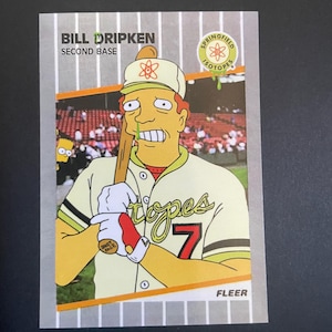 Puede incluir: Una tarjeta de béisbol con Bill Dripken, segunda base de los Springfield Isotopes. La tarjeta muestra un personaje de dibujos animados con uniforme de béisbol sosteniendo un bate. La tarjeta tiene un fondo gris con líneas verticales blancas y el logo de Fleer.