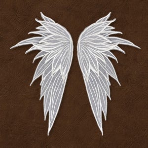 Op de afbeelding: Twee witte, delicate, kanten engelen vleugels met ingewikkelde aderachtige details. De vleugels zijn symmetrisch, met een gelaagd ontwerp en puntige uiteinden. De achtergrond is een effen, getextureerde bruine kleur.