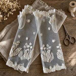 May include: A pair of sheer white fingerless gloves made of fine tulle fabric, featuring intricate ivory floral embroidery and scalloped lace trim at the edges. The delicate botanical patterns are scattered across the surface of the gloves.