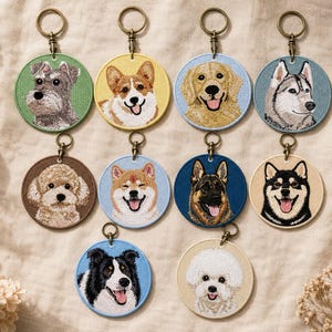 May include: A collection of embroidered dog breed keychains. Each keychain features a different dog breed portrait, including a Schnauzer, Corgi, Golden Retriever, and Husky. The keychains have a circular shape with a metal ring.