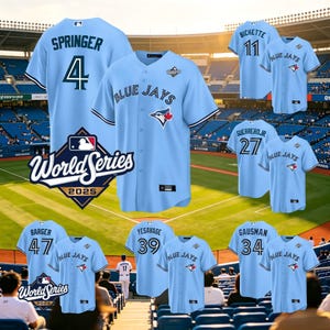 Puede incluir: Camisetas de béisbol azul claro con el texto "BLUE JAYS" y nombres y números de jugadores. Las camisetas tienen un logotipo del equipo y las palabras "World Series 2025". Las camisetas se muestran frente a un estadio de béisbol.