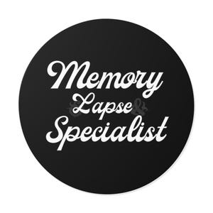 May include: A black circular sticker with white text that reads "Memory Lapse & Specialist" in a stylized font. The text is arranged in three lines, with "Memory" at the top, "Lapse &" in the middle, and "Specialist" at the bottom.