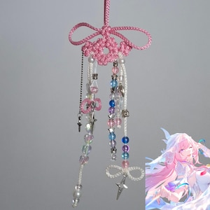 Könnte beinhalten: Ein handgefertigter rosa Charm mit einem dekorativen Blumendesign und herabhängenden Perlensträngen. Der Charm hat klare, rosa, blaue und silberne Perlen sowie kleine Stern- und Kreuzanhänger. Die Oberseite hat eine rosa Schleife und eine Schlaufe zum Aufhängen.