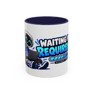 May include: A white ceramic mug with a dark blue interior and rim. The exterior features a graphic of a robot character sitting with a laptop, accompanied by the text "WAITING FOR REQUIREMENTS" in blue and white, along with a loading bar graphic.