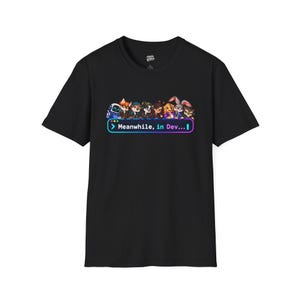 Könnte beinhalten: Ein schwarzes Kurzarm-T-Shirt mit einem Grafikdruck verschiedener Zeichentrickfiguren, die in einer Reihe über einem bunten rechteckigen Rahmen stehen, der den weißen Text "Meanwhile, in Dev..." mit einem blinkenden Cursor enthält.