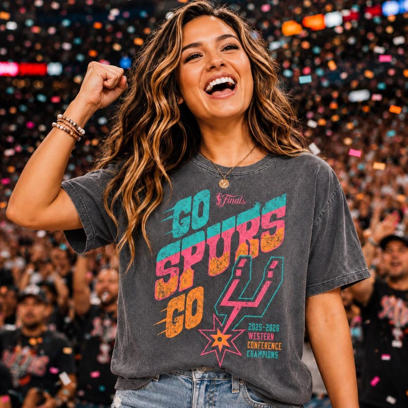 May include: A charcoal gray short-sleeve t-shirt featuring a distressed graphic print that reads GO SPURS GO with the San Antonio Spurs logo, the text 2025-2026 WESTERN CONFERENCE CHAMPIONS, and a small NBA Finals logo in pink, orange, and teal colors.