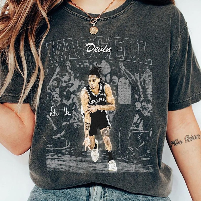 K&ouml;nnte beinhalten: Ein anthrazitfarbenes Kurzarm-T-Shirt mit einem Grafikdruck des Basketballspielers Devin Vassell im Trikot der San Antonio Spurs. Das Design zeigt den Schriftzug VASSELL, Devin sowie eine Unterschrift vor einem verblassten Hintergrund.