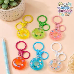 May include: A collection of colorful donut-shaped keychains. Each keychain features a clear, circular design with small decorative elements inside. The keychains come in various colors, including yellow, green, pink, orange, blue, and white, with matching colored clasps.