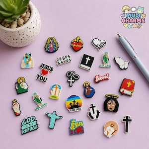 Könnte beinhalten: Eine Sammlung farbenfroher religiöser Charms mit verschiedenen Designs, darunter Kreuze, Herzen und Bilder von Heiligen. Einige Charms zeigen Texte wie "Jesus Saves", "Blessed" und "God is my Refuge". Die Charms sind auf einer hellvioletten Oberfläche verstreut.