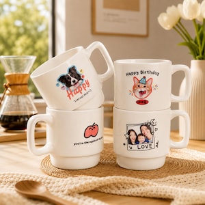 Può includere: Quattro tazze di ceramica bianca impilate. Ogni tazza presenta un design diverso: un cane con la parola "Happy", un gatto con "Happy Birthday", una mela con il testo "you're the apple of my" e una foto di famiglia con la parola "LOVE".