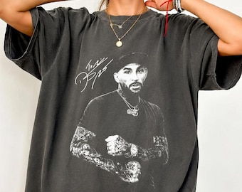 May include: A charcoal gray oversized t-shirt featuring a black and white graphic print of a bearded man wearing a cap and a chain. The print includes a stylized signature above the man's head. The shirt has short sleeves and a crew neckline.
