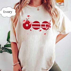 May include: Ivory-colored t-shirt with a red graphic design featuring three stylized circles and horizontal lines, accented with red floral branches and blossoms. The word "Ivory" is in a white cloud-shaped text box.
