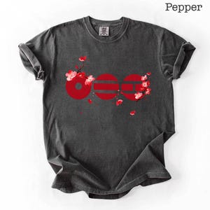 May include: Dark grey t-shirt with a red graphic design featuring the word "OOO" and floral accents. The shirt has a crew neck and short sleeves. The word "Pepper" is printed at the top right.