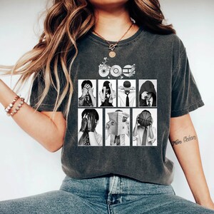May include: Dark gray t-shirt featuring a graphic design with the word "60s" above a grid of black and white images of people covering their faces. The shirt is made of a soft, comfortable material.