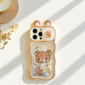Puede incluir: Funda de teléfono beige y blanca con un diseño de oso de dibujos animados. La funda tiene una sección de líquido transparente con purpurina y orejas de oso en 3D en la parte superior. También hay una pequeña bebida en 3D.