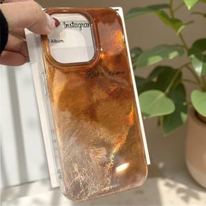 May include: A clear phone case with a shimmering, golden-brown design. The case has the word "Instagram" and "Album" printed on it. The words "Retro time" are also printed on the case.