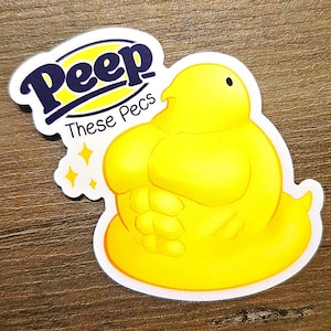 May include: A yellow Peep marshmallow character with a muscular physique. The Peep is wearing a white outline and has a blue text bubble that says "These Pecs".