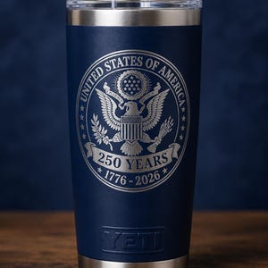 May include: Navy blue insulated tumbler with a silver rim and base. The tumbler features the engraved text "UNITED STATES OF AMERICA" around a detailed eagle emblem. Below the emblem is "250 YEARS 1776-2026". The brand name "YETI" is at the bottom.
