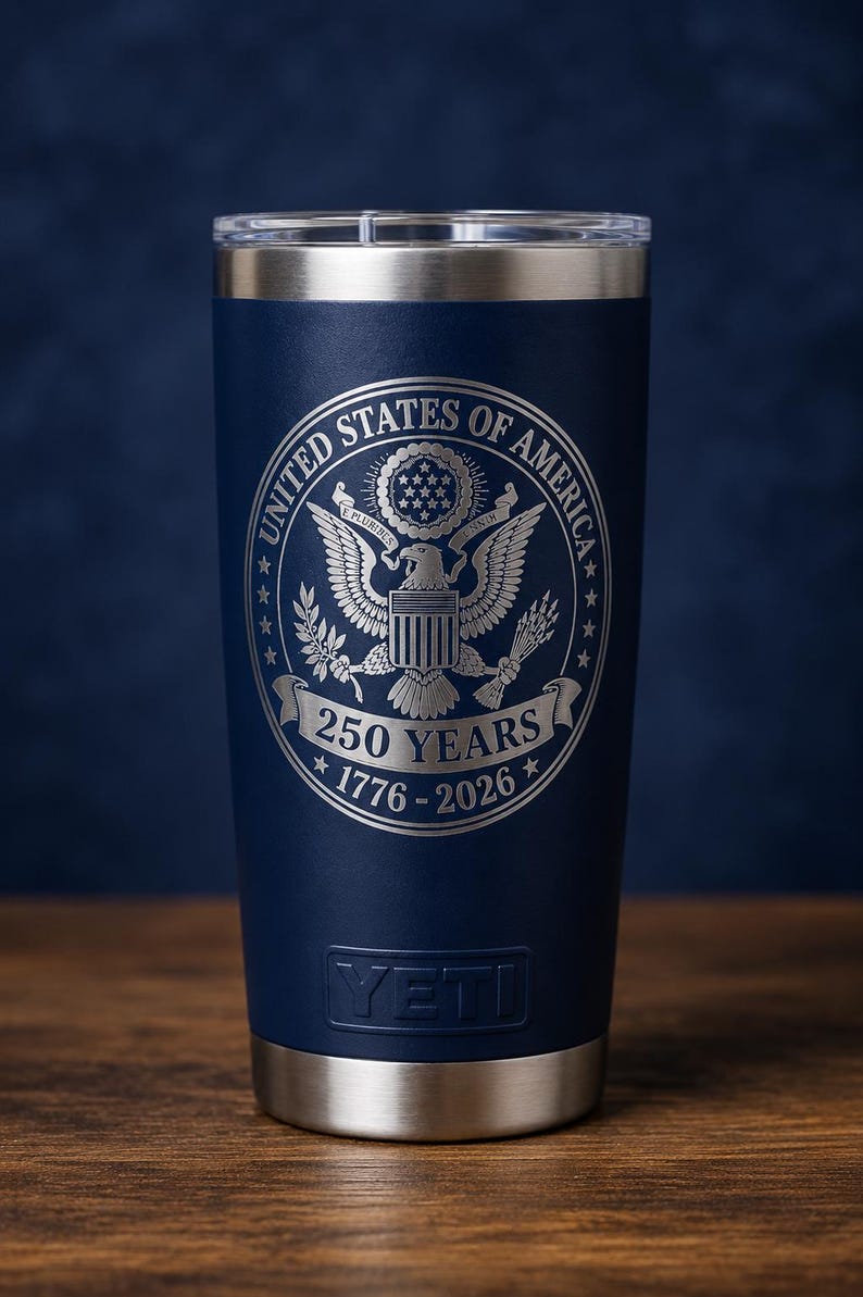 May include: Navy blue insulated tumbler with a silver rim and base. The tumbler features the engraved text "UNITED STATES OF AMERICA" around a detailed eagle emblem. Below the emblem is "250 YEARS 1776-2026". The brand name "YETI" is at the bottom.
