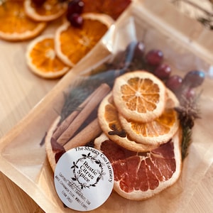 May include: A clear bag filled with dried orange and grapefruit slices, cranberries, cinnamon sticks, and whole cloves. The bag has a white label with the text "Rustic Citrus Spice" and "The Shaggy Coo Farmery".
