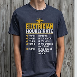 Può includere: Una maglietta blu scuro con una grafica divertente che recita "Electrician Hourly Rate" e elenca diversi tariffe in base al livello di assistenza fornito. La grafica include un fulmine stilizzato e un pugno.