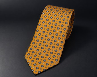 May include: A mustard yellow necktie featuring a repeating geometric pattern of small dark blue and white squares. The tie has a pointed tip and a smooth, folded construction, displaying a consistent, symmetrical design across the entire surface.