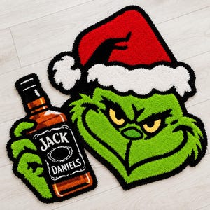 Könnte beinhalten: Ein getufteter Teppich in Form einer grünen Figur mit einer rot-weißen Weihnachtsmütze, die eine braune Flasche mit einem schwarz-weißen Etikett mit der Aufschrift JACK DANIELS hält. Der Teppich hat kräftige schwarze Konturen.