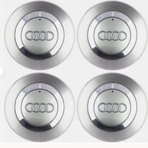 May include: Four silver Audi wheel centre caps. Each cap features the Audi logo, a set of four interlocking rings, in the centre. The caps have a circular design with a polished, reflective finish.