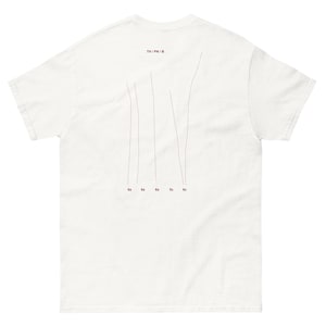 Puede incluir: Camiseta blanca con un diseño minimalista. La parte trasera de la camiseta presenta líneas grises verticales finas y números pequeños. El texto "TH / PN / B" está impreso en rojo oscuro en la parte superior.