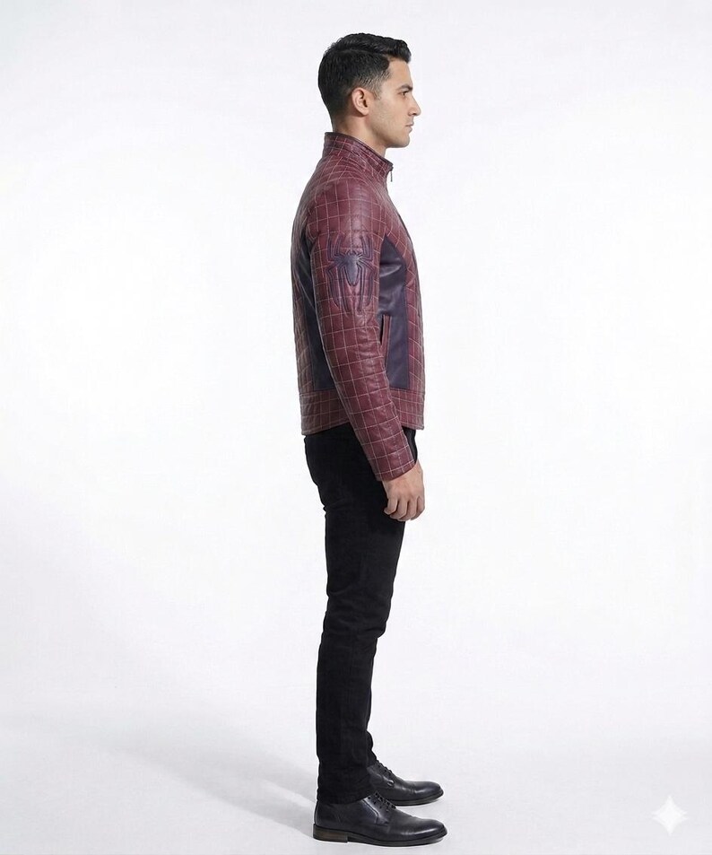 Peut inclure: Une veste en cuir bordeaux avec un motif &agrave; carreaux, un col montant et un embl&egrave;me d'araign&eacute;e bleu fonc&eacute; sur la manche. La veste est port&eacute;e avec un pantalon noir et des chaussures de ville en cuir noir, vue de profil.