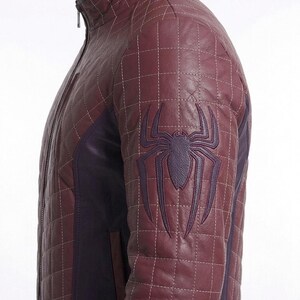 Peut inclure: Une veste matelass&eacute;e bordeaux dot&eacute;e d'un col montant, d'une fermeture &eacute;clair int&eacute;grale et d'un embl&egrave;me d'araign&eacute;e violet fonc&eacute; en relief sur la manche. La veste pr&eacute;sente un motif de surpiq&ucirc;res en forme de grille sur les panneaux bordeaux.