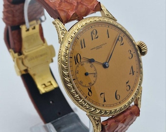 May include: A gold wristwatch with a textured, rope-patterned bezel and a tan dial featuring black Arabic numerals. The watch has a small sub-dial for seconds and a brown, scale-textured leather strap with a gold-toned metal deployment clasp.