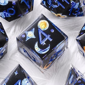 Puede incluir: Un juego de dados poliédricos de resina negra con diseños celestiales incrustados que incluyen estrellas, lunas y planetas. Los números están pintados en un color azul brillante. Los dados tienen un acabado brillante y están agrupados.