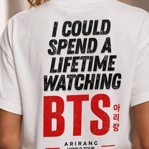 Peut inclure: T-shirt blanc avec l'inscription "I COULD SPEND A LIFETIME WATCHING BTS" en noir, police vieillie. Le mot "BTS" est en rouge, avec des caract&egrave;res cor&eacute;ens et "ARIRANG WORLD TOUR" en dessous.