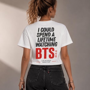 Peut inclure: T-shirt blanc avec l'inscription noire "I COULD SPEND A LIFETIME WATCHING BTS" et "BTS" en rouge avec des caract&egrave;res cor&eacute;ens. En dessous, il est &eacute;crit "ARIRANG WORLD TOUR". Le t-shirt est port&eacute; avec un jean noir.