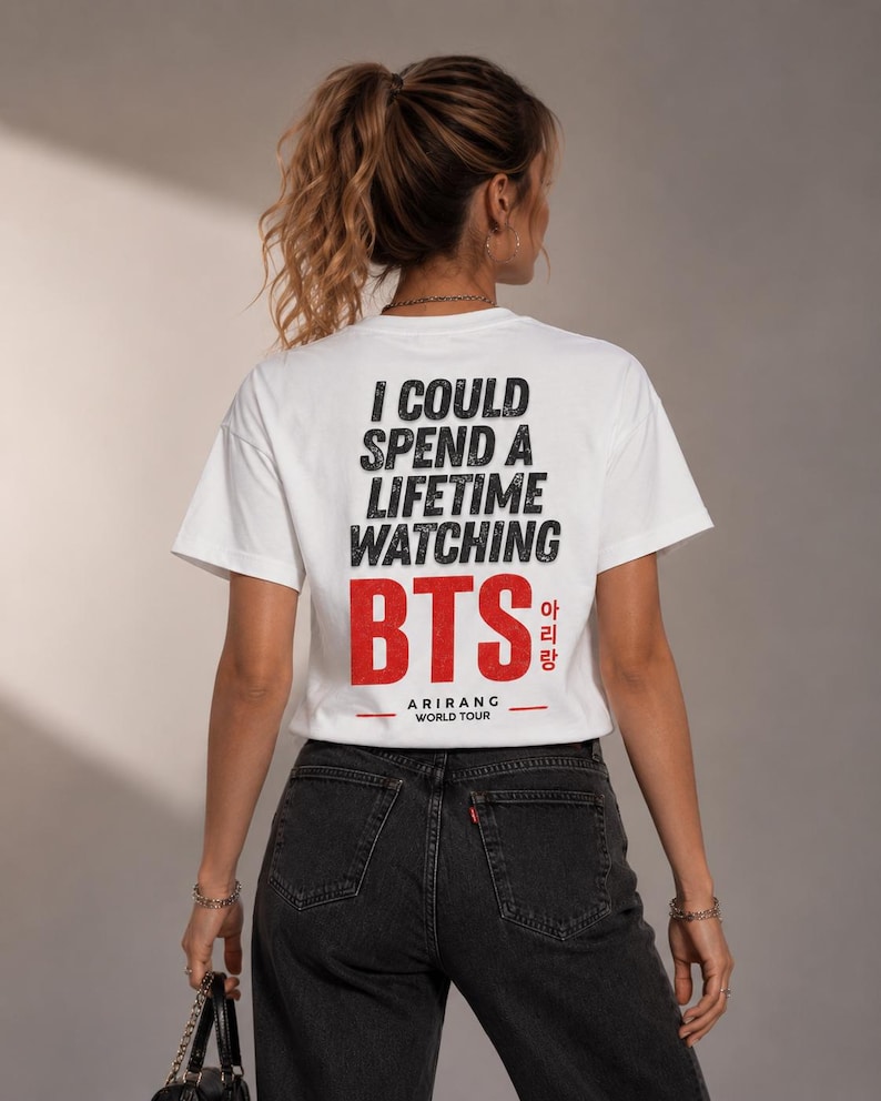 Peut inclure: T-shirt blanc avec l'inscription noire "I COULD SPEND A LIFETIME WATCHING BTS" et "BTS" en rouge avec des caract&egrave;res cor&eacute;ens. En dessous, il est &eacute;crit "ARIRANG WORLD TOUR". Le t-shirt est port&eacute; avec un jean noir.