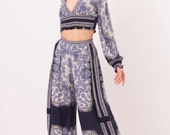 May include: A two-piece set consisting of a long-sleeved cropped top with a deep V-neckline and wide-leg trousers. Both pieces feature a dark blue and white paisley pattern with a smocked waistband on the top and a high-waisted fit on the pants.