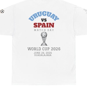 Può includere: T-shirt bianco con la scritta "URUGUAY vs SPAIN MATCH DAY" in blu e rosso, con una grafica della Coppa del Mondo. La maglietta include anche il testo "WORLD CUP 2026" e la data "JUNE 26, 2026 GUADALAJARA".