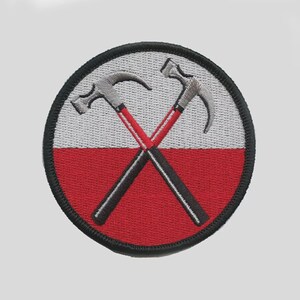 May include: A circular embroidered patch featuring a split background of light gray on the top half and red on the bottom half. Two hammers with silver heads and red and black handles are crossed in the center, all enclosed by a thick black border.
