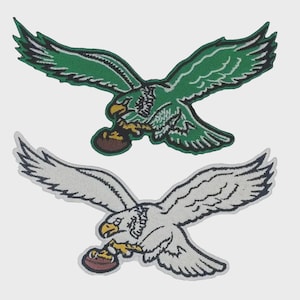 May include: Two embroidered patches featuring an eagle in flight with wings spread wide. One patch is green with white and black details, and the other is white with black and grey details. Both eagles have yellow beaks and hold a brown football.